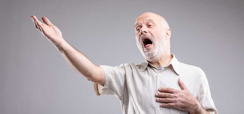 We see an older man singing, with his arms dramatically outstretched.