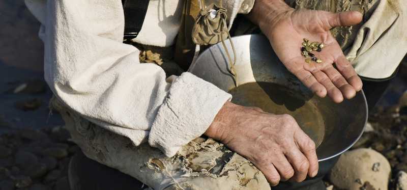 Part of a person is shown, by water, having successfully panned for gold.