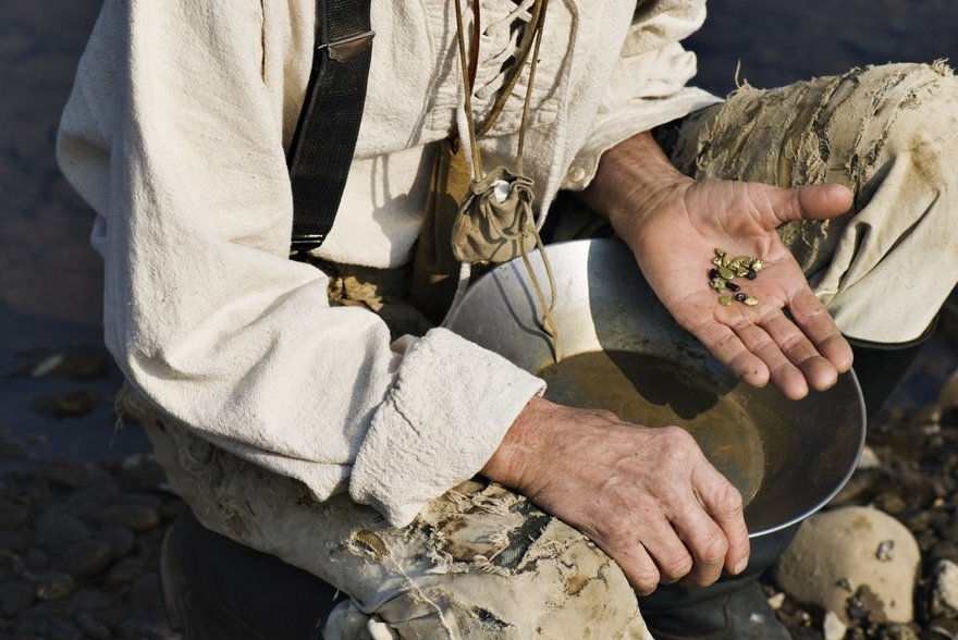 Part of a person is shown, by water, having successfully panned for gold.