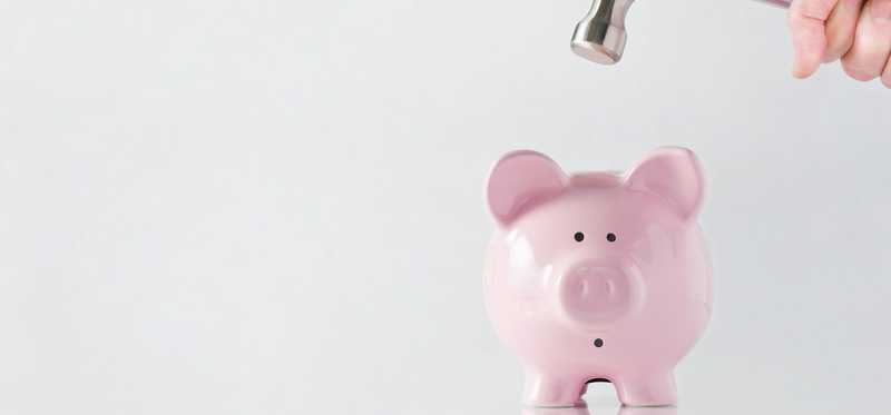 A hand with a hammer about to hit and break a piggy bank.