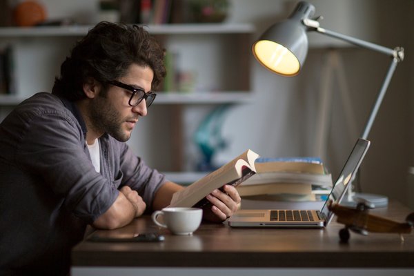 A person sitting and reading a book by lamplight.
