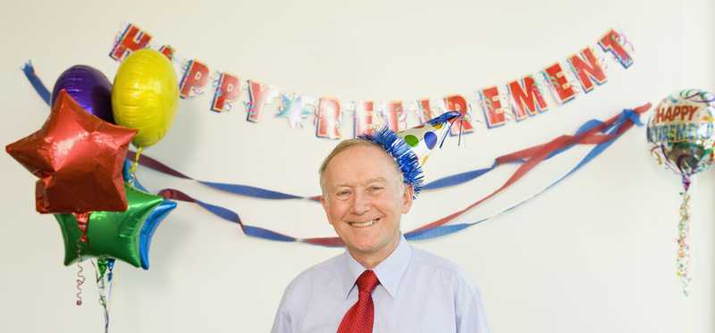 Person smiling and standing under a banner that says Happy Retirement.
