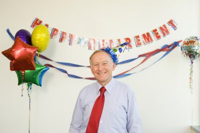 Person smiling and standing under a banner that says Happy Retirement.