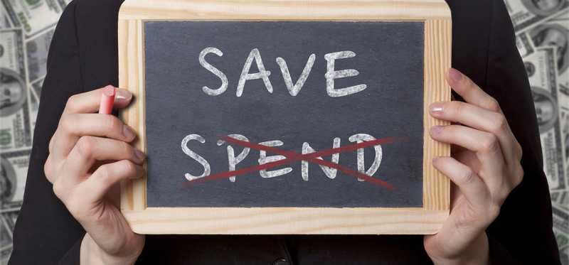 Hands holding a small chalkboard with the words Spend and Save, with Spend crossed out