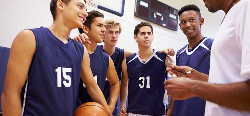 We see a coach talking to a handful of young male basketball players.