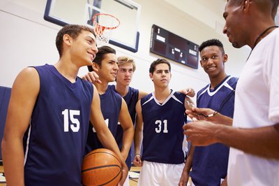 We see a coach talking to a handful of young male basketball players.