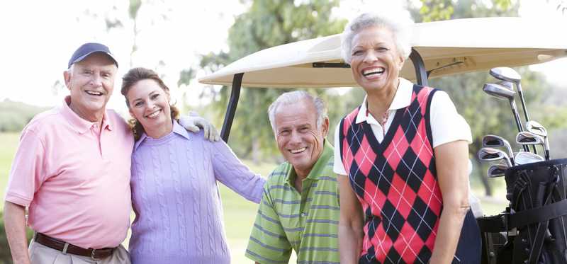 Four people smiling while standing by a golf cart.