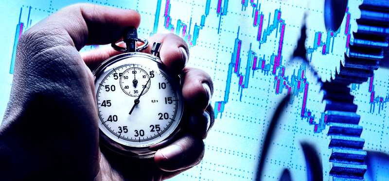 A hand is holding a stopwatch against a backdrop of a stock chart.