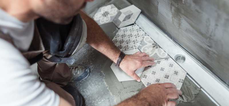 Person tiling a floor in a home bathroom.