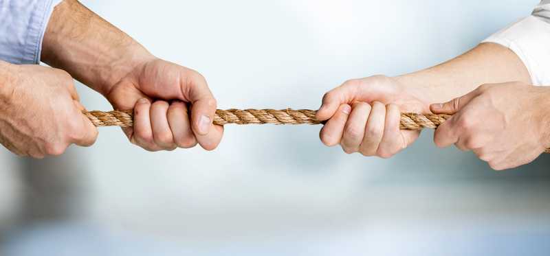 Two people's hands engaged in a tug-of-war with a rope.