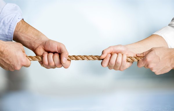 Two people's hands engaged in a tug-of-war with a rope.