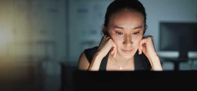 A person is staring at a laptop and resting their head in their hands.
