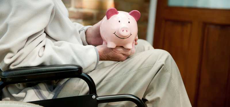 Person who uses wheelchair is holding piggy bank.