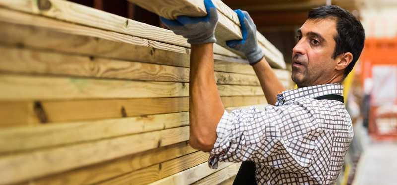 A worker in a store is lifting some lumber off a shelf.