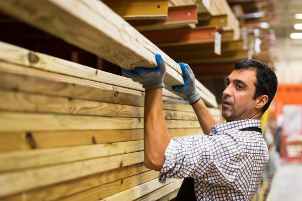 A worker in a store is lifting some lumber off a shelf.