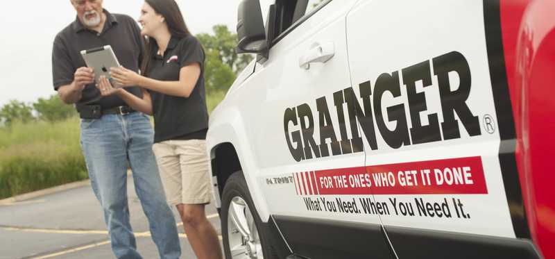 Two people are standing by a truck labeled Grainger.