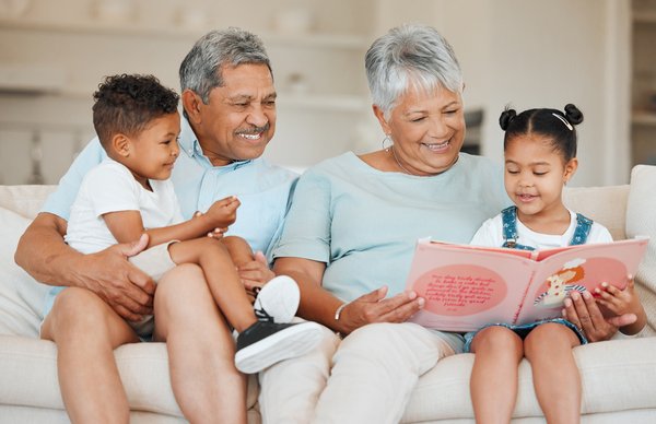 Grandparents read to their grandkids sitting on a couch.