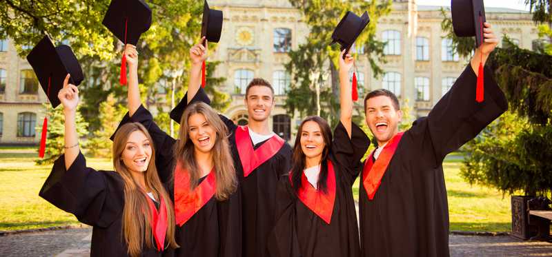 Group of college grads holding caps in the air.