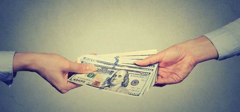 Two hands exchange a pile of cash.