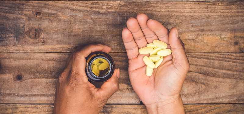 Hands holding some pills from a bottle over a wooden surface.