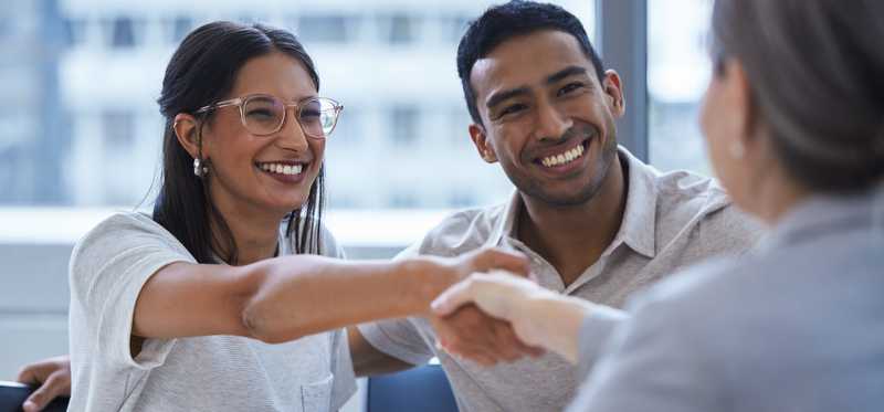 A smiling couple shakes the hand of a finance professional.