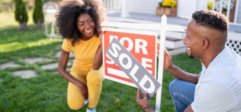 A happy couple adds the Sold sign to the For Sale sign in front of a home.