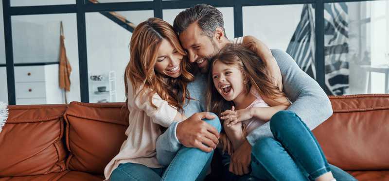 A happy couple hugs their child on their living room couch.