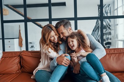 A happy couple hugs their child on their living room couch.