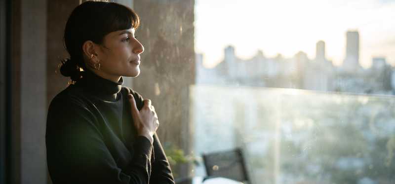 Person smiling while looking out an apartment window at a city skyline.