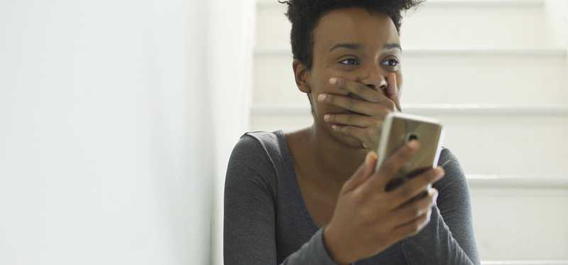 Person sitting on stairs and holding a phone looks happily surprised.