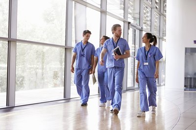 Healthcare workers walking together inside a medical facility wearing blue scrubs.