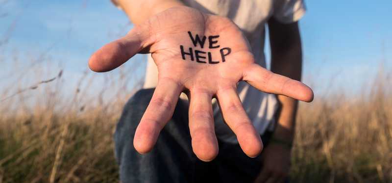 Person holding out their hand with the words We Help on it.