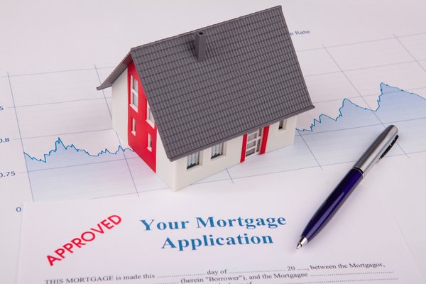An approved mortgage application next to a small model home and line graph.