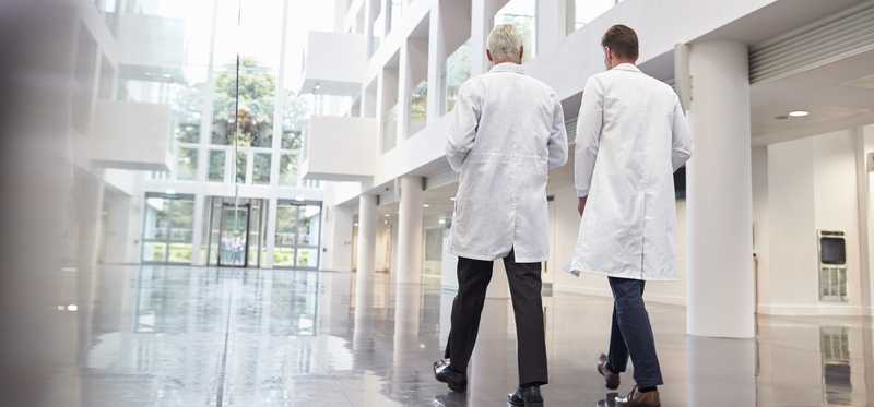 Two doctors in white coats walk in hallway of a hospital.