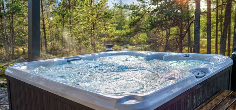 A bubbling hot tub sitting outside next to trees with the sun peaking through the tree branches.