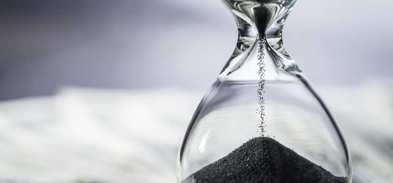 Hourglass with sand on top of spread-out cash.