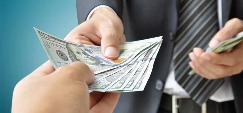 man in business suit handing stack of hundred dollar bills to another person