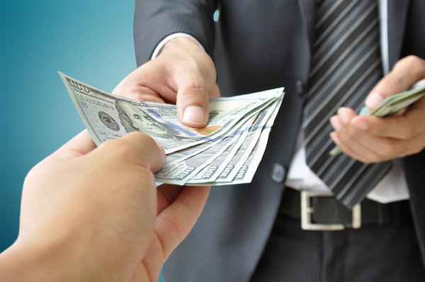 man in business suit handing stack of hundred dollar bills to another person