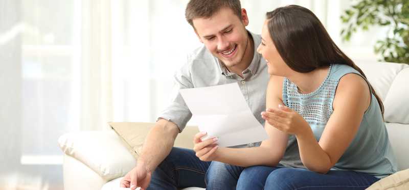 Two people sitting on a couch and looking at papers together.