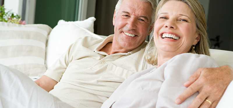 mature man and woman sitting on couch with their arms around each other and smiling