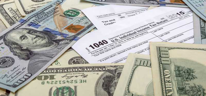 Pile of hundred dollar bills and an IRS form 1040.