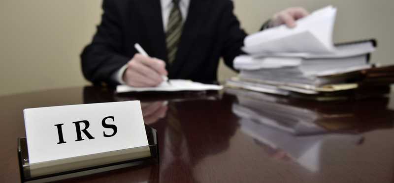 A businessperson working on paperwork behind a desk with business cards that say IRS.