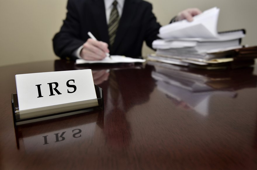 A businessperson working on paperwork behind a desk with business cards that say IRS.