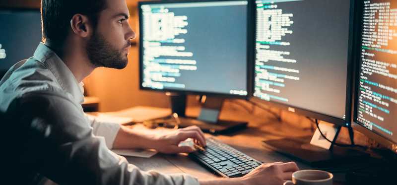 IT professional looking at three computer screens