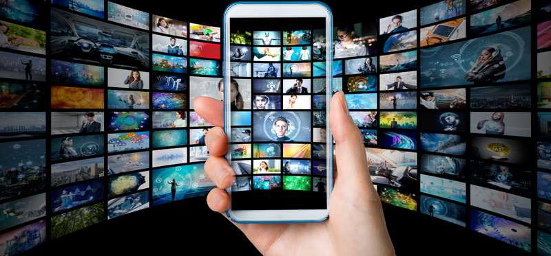 A phone being held in front of a screen showing various movies and tv shows.