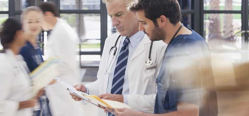 Physician review contents of a folder with another person in scrubs.