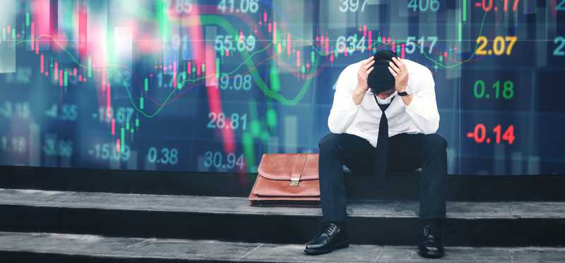 An upset businessman sits in front of a screen showing plunging stock prices.