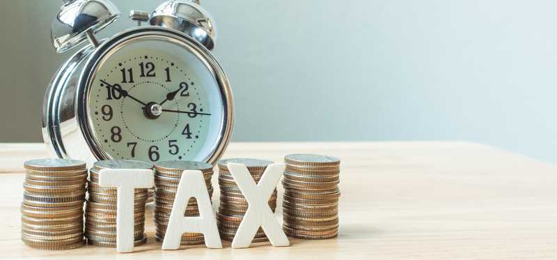 The word tax in front of coin piles and an alarm clock.