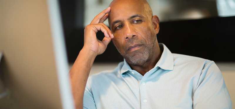 Serious person sitting back and thinking at a computer desk.