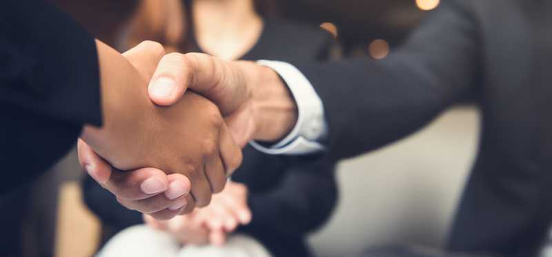 Two men in suits shake hands.